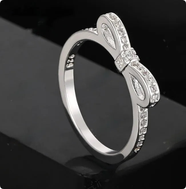Silver electroplated bow-shaped ring with zircon crystal stones on a finger.