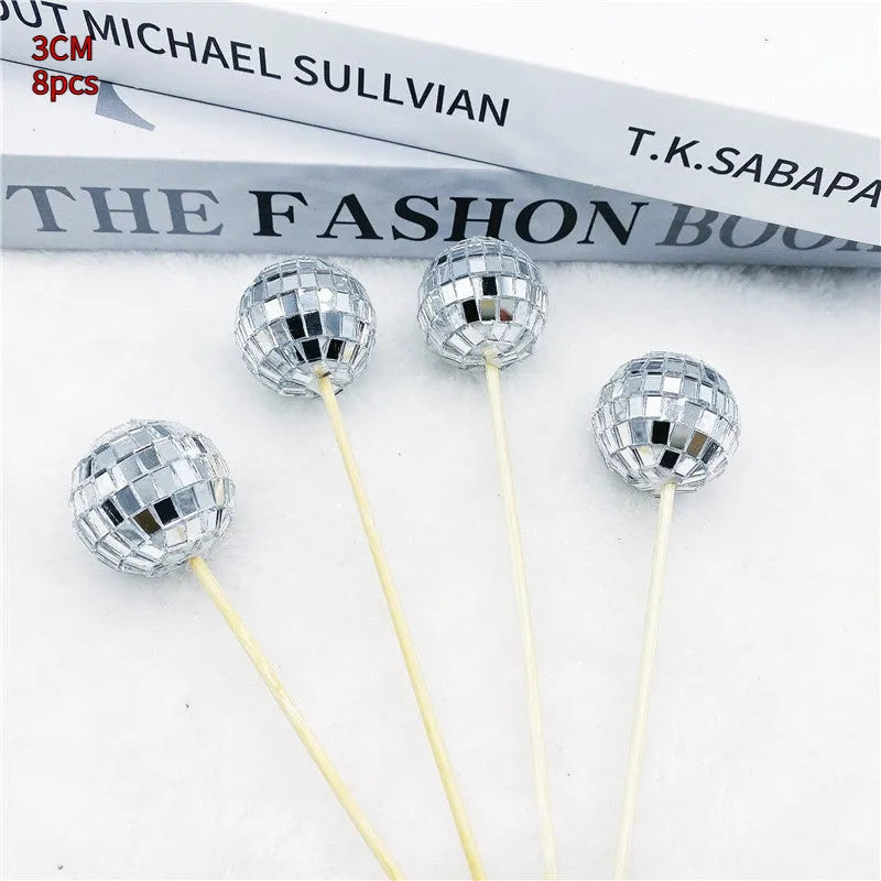 Glass mirror ball cake decoration on a wooden stick, showing reflective surface.