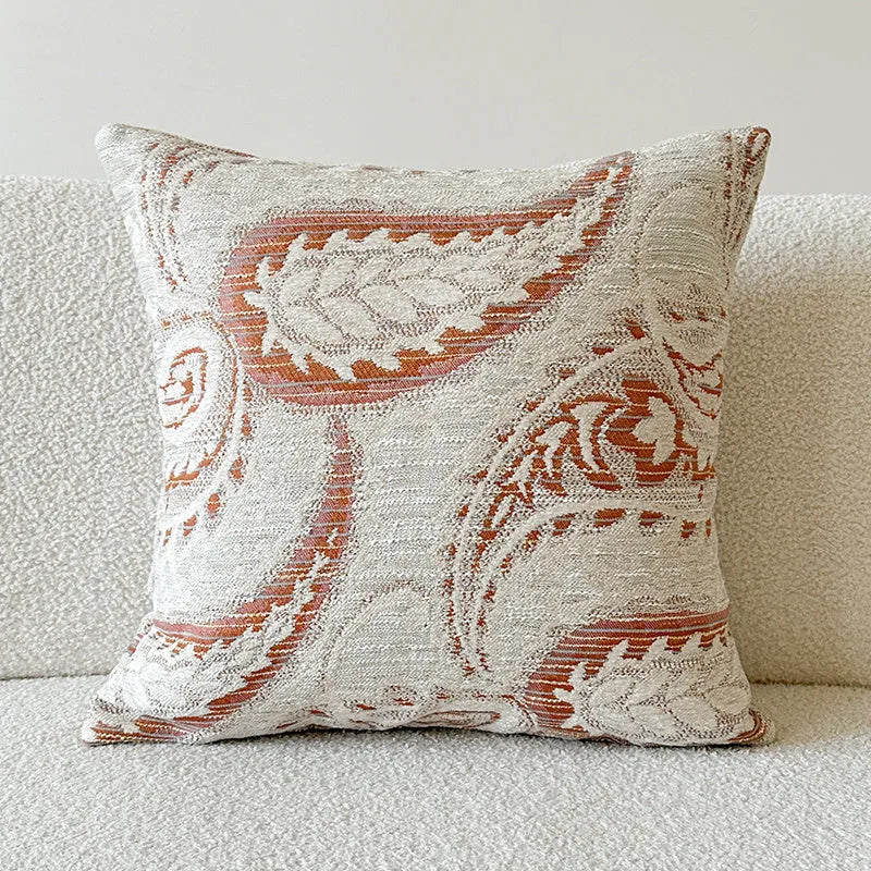 Amber-coloured jacquard pillow cover with paisley and flower pattern, shown in 45x45cm size on a sofa.