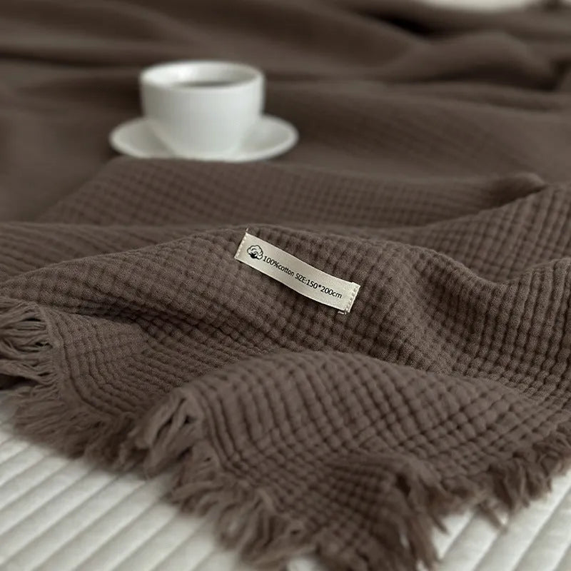 Four-layer gauze cotton blanket with tassel trim in avocado green colour draped over a sofa