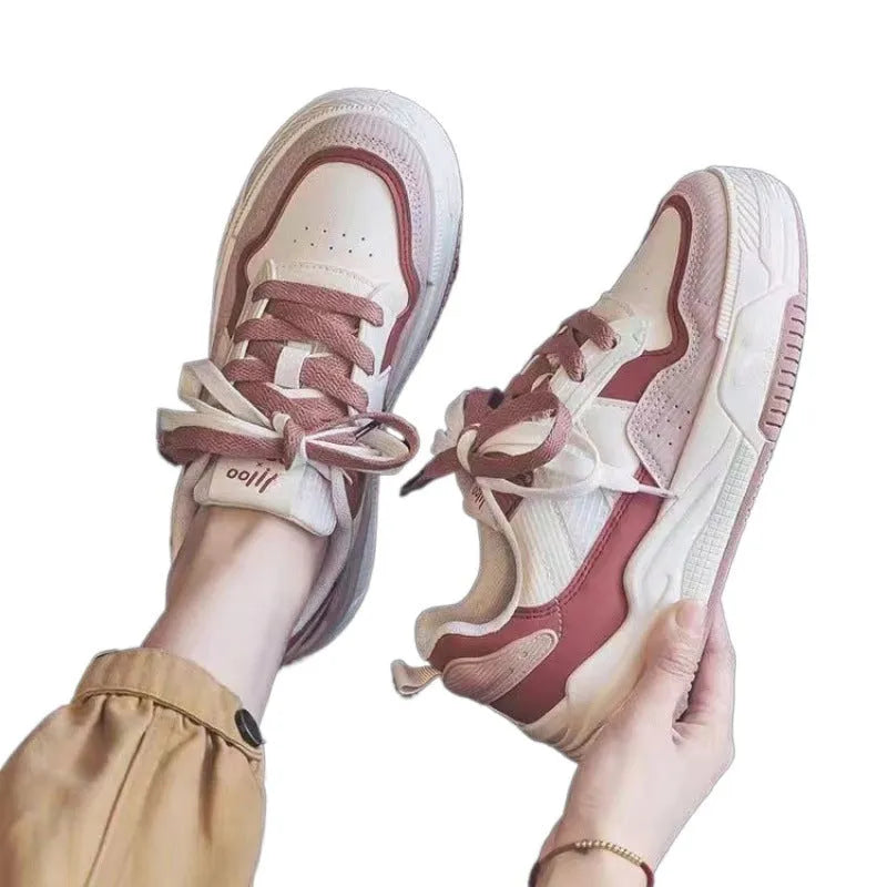 Women's pink and white low top imitation leather sneaker with rubber sole on a neutral background.