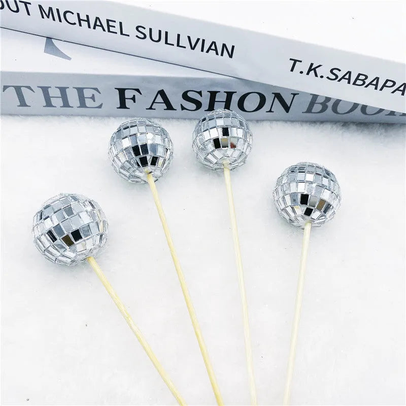 Glass mirror ball cake decoration on a wooden stick, showing reflective surface.