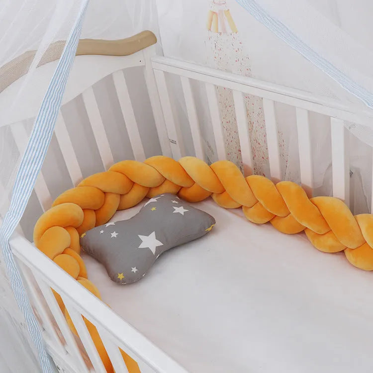 Braided knot style baby crib bumper in a light grey colour, shown lined inside a white wooden cot.