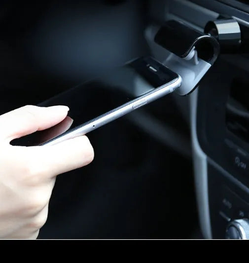 Black universal gravity car phone holder with 360-degree rotating head on a car dashboard.