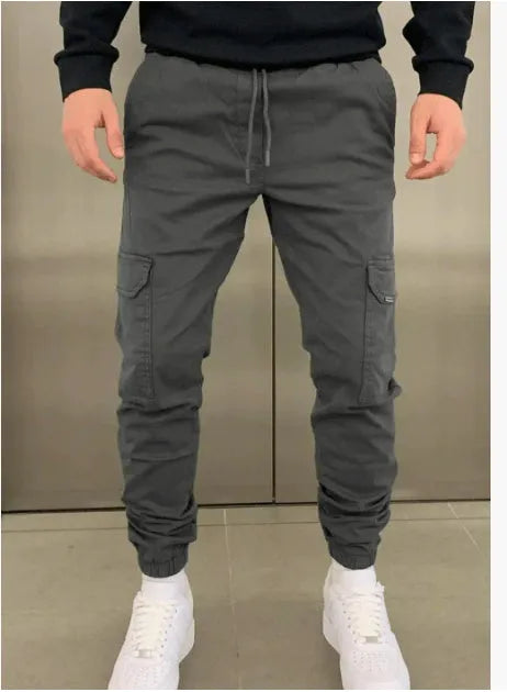 Man wearing loose light blue casual trousers with patch pockets and an elasticated waist.