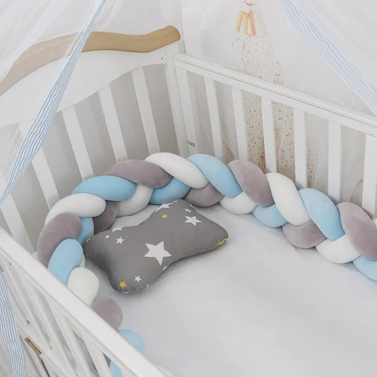 Braided knot style baby crib bumper in a light grey colour, shown lined inside a white wooden cot.