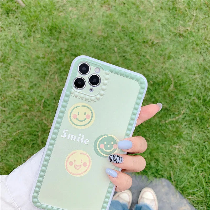 Green TPU iPhone case with geometric smiley face and polka dot frame design on a table.