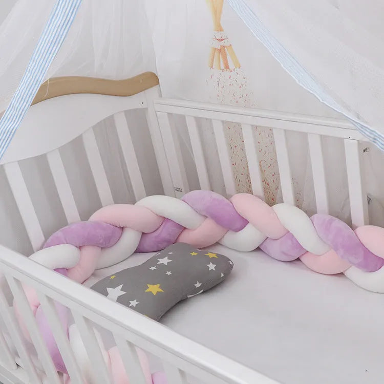Braided knot style baby crib bumper in a light grey colour, shown lined inside a white wooden cot.