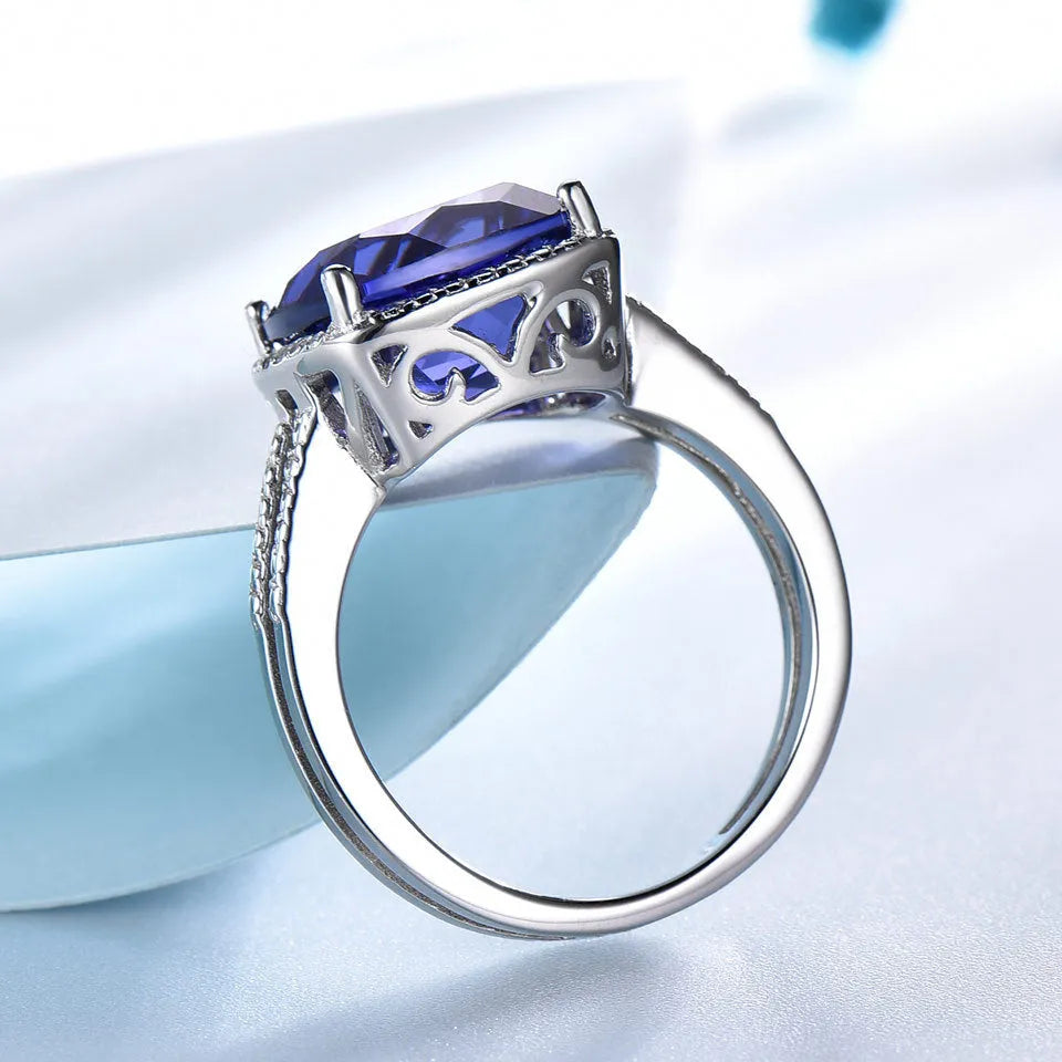Women's sterling silver ring with oval blue Tanzanite gemstone on a finger.