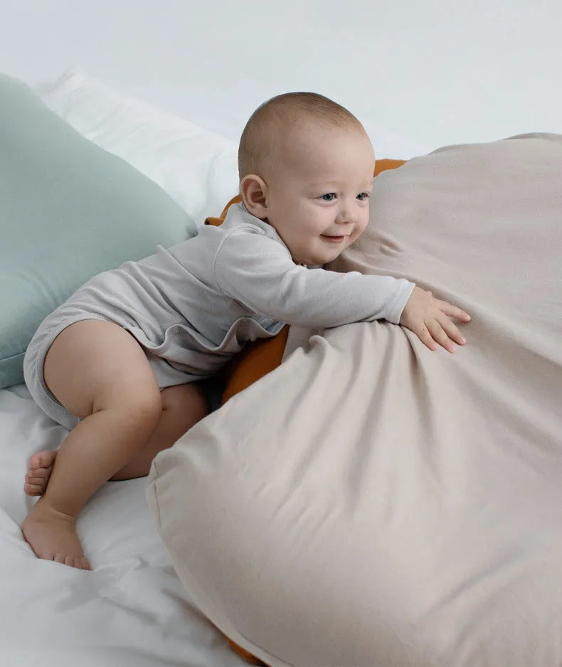 Beige portable baby nest crib cot for newborn infant on a bed