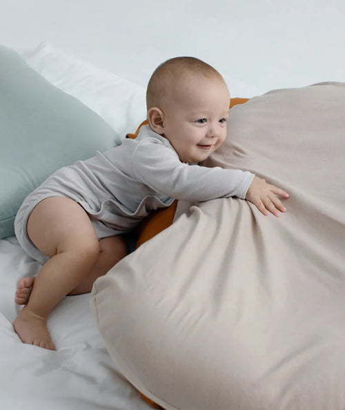 Beige portable baby nest crib cot for newborn infant on a bed