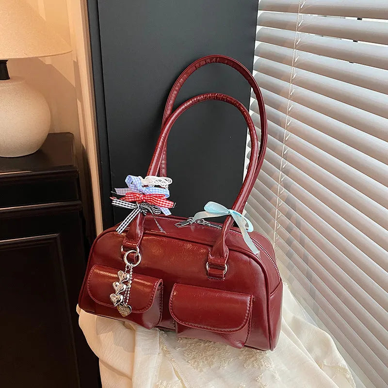 Retro women's black PU leather pillow-shaped shoulder bag with flap and double straps, shown with optional ribbon pendant.