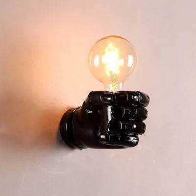 Decorative resin wall lamp sculpted as a clenched fist, available in black, white, and wood grain finishes.