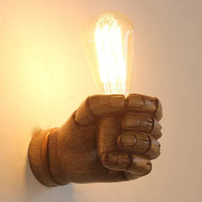 Decorative resin wall lamp sculpted as a clenched fist, available in black, white, and wood grain finishes.