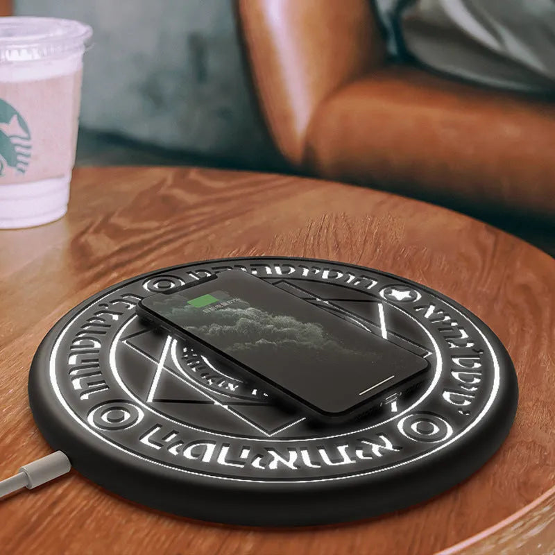 Black 10W fast wireless phone charger with glowing magic array pattern on a desk.