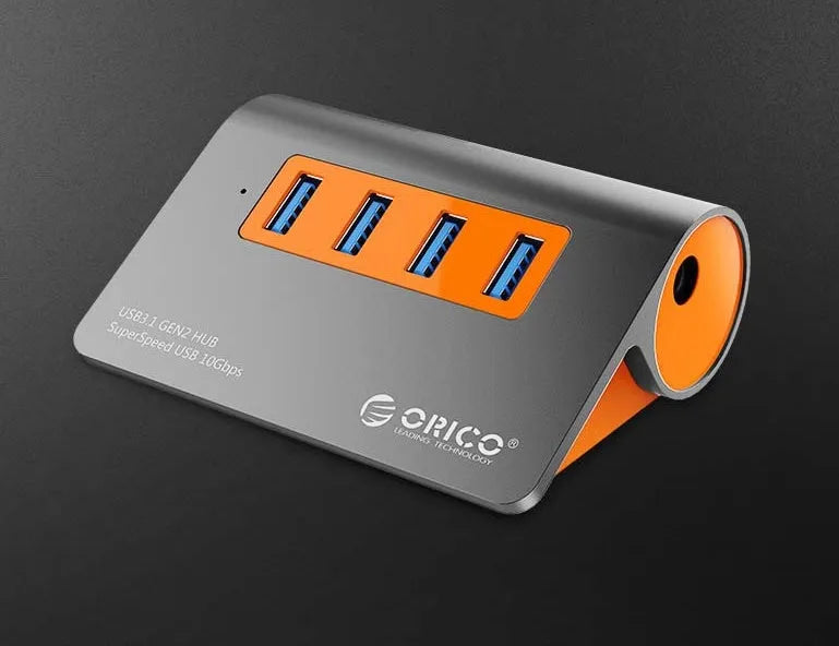 Dark grey aluminium USB-C hub with four USB 3.1 ports, orange trim, external power input, and a separate cable.