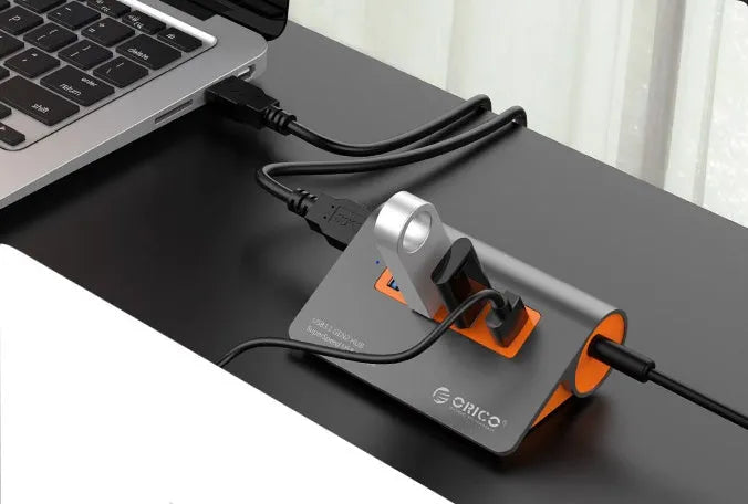 Dark grey aluminium USB-C hub with four USB 3.1 ports, orange trim, external power input, and a separate cable.