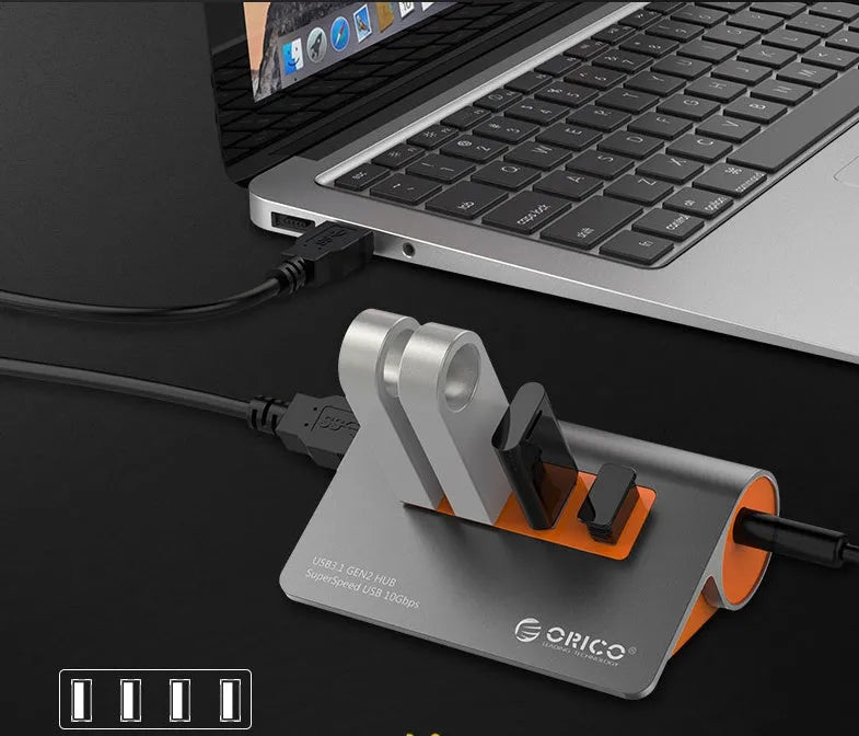 Dark grey aluminium USB-C hub with four USB 3.1 ports, orange trim, external power input, and a separate cable.