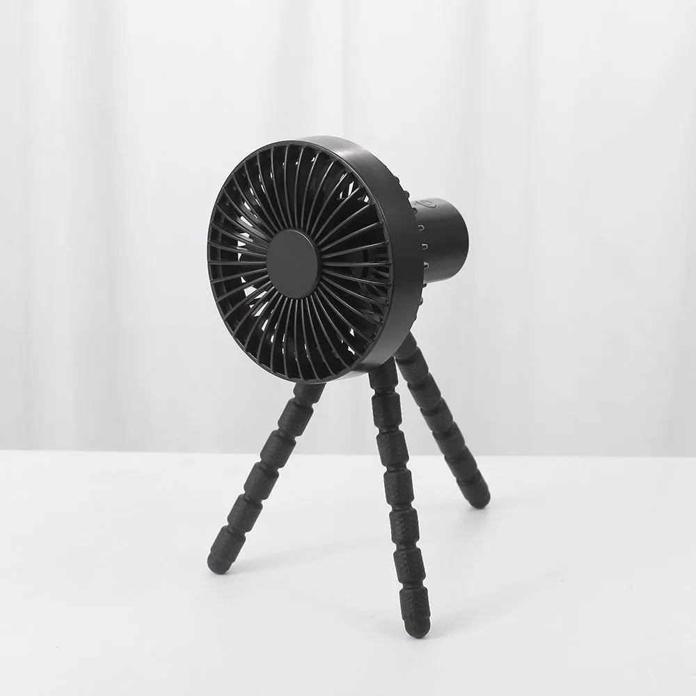Black flexible tripod USB desktop fan with automatic head shake, shown on a desk next to a laptop.
