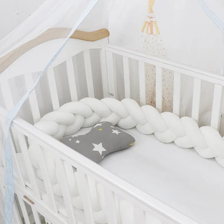 Braided knot style baby crib bumper in a light grey colour, shown lined inside a white wooden cot.