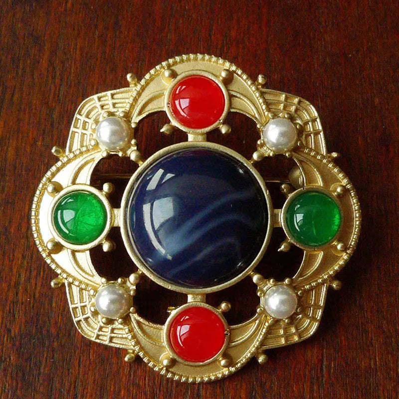 Close-up of a vintage baroque style zinc alloy brooch with a diamond shape on a dark fabric background.