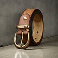 Men's black genuine cowhide leather belt with copper pin buckle on a jeans background.