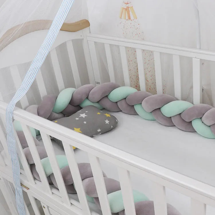 Braided knot style baby crib bumper in a light grey colour, shown lined inside a white wooden cot.