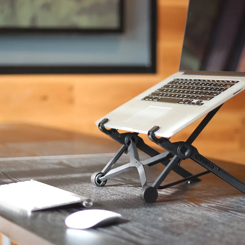 Black folding portable laptop stand made of reinforced nylon, shown both open for use and folded flat.