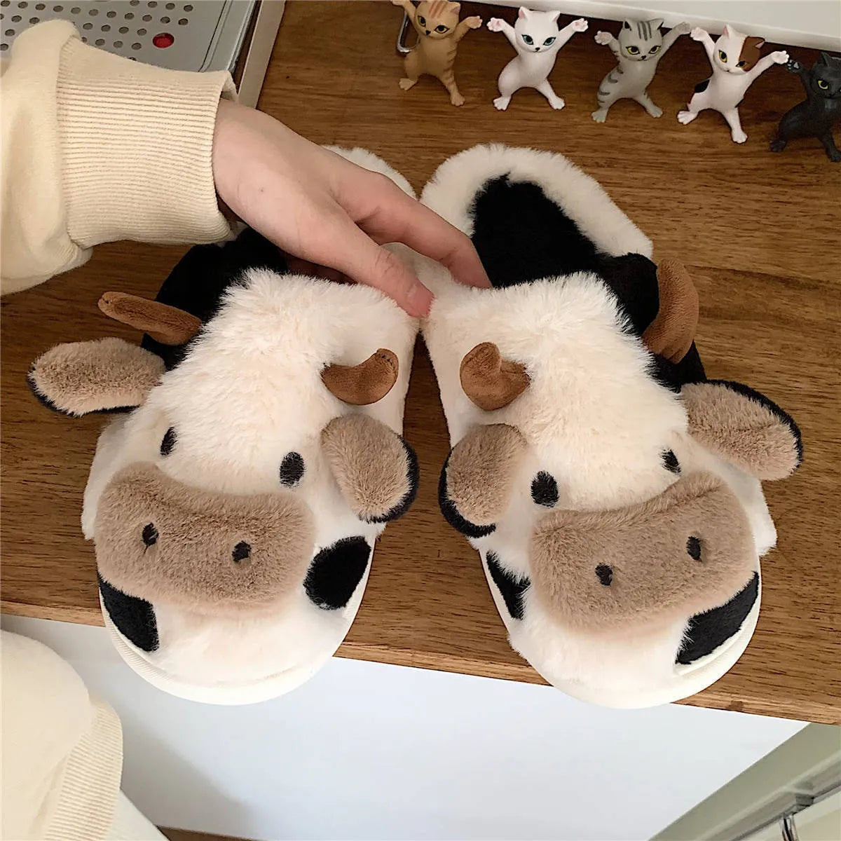 White cow-themed faux fur slippers with plush lining and textured non-slip soles.