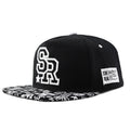 Cotton baseball cap with embroidered letters in black or white, showing adjustable strap.