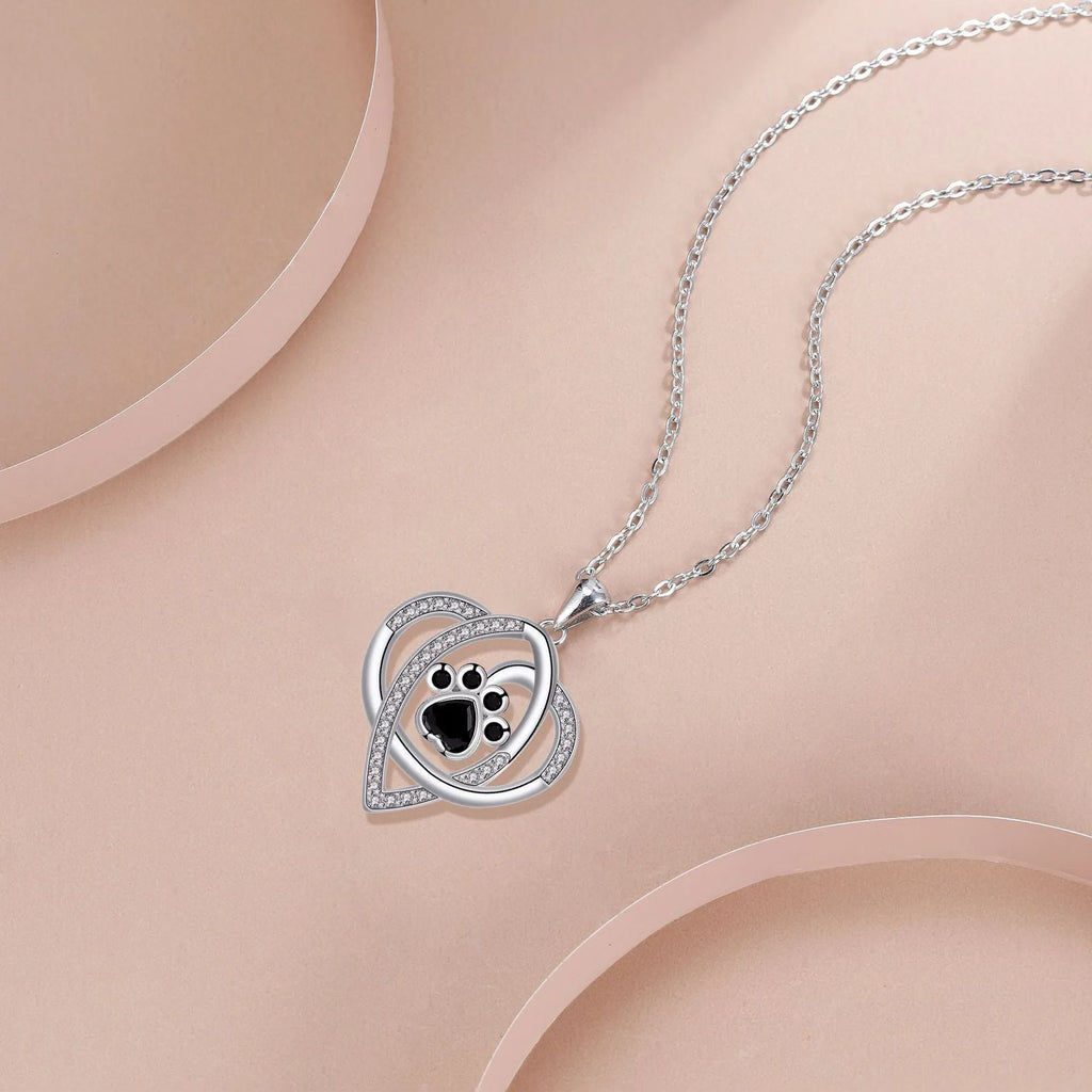 Close-up of a copper necklace pendant showing detailed cat and dog paw prints on a cross chain.