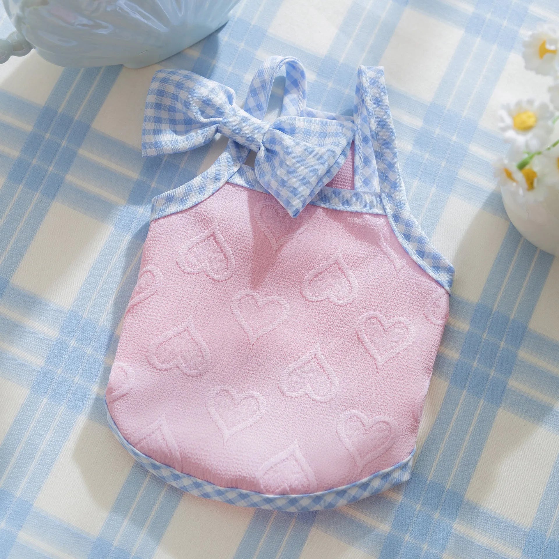Small dog wearing a blue vest with suspenders and a heart-shaped bow, showing elastic sides.