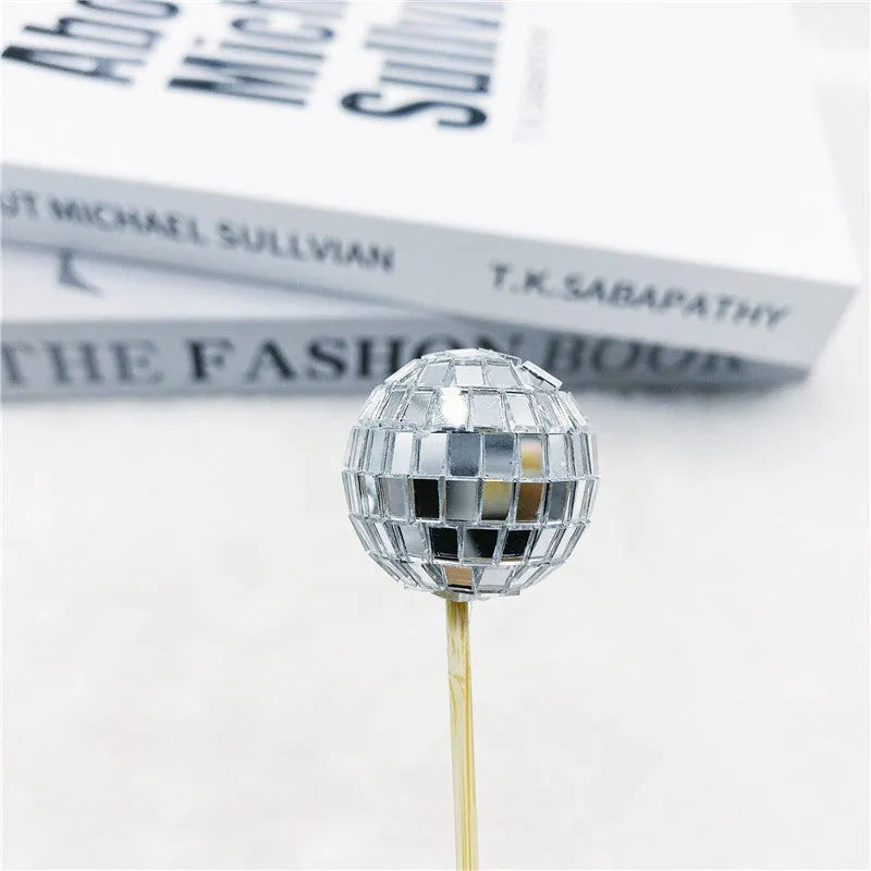 Glass mirror ball cake decoration on a wooden stick, showing reflective surface.