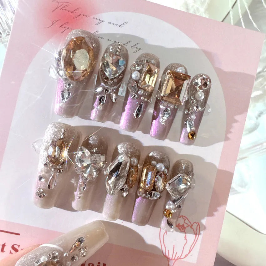 False nail patches with large rhinestones on card, shown with jelly adhesive pot and nail tools.