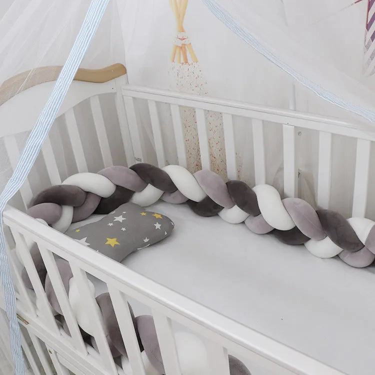 Braided knot style baby crib bumper in a light grey colour, shown lined inside a white wooden cot.