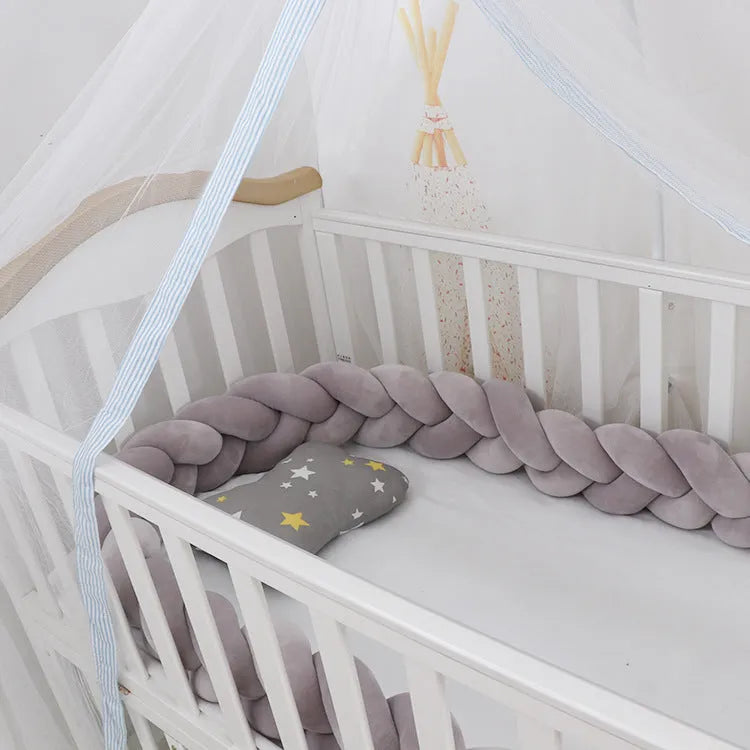 Braided knot style baby crib bumper in a light grey colour, shown lined inside a white wooden cot.