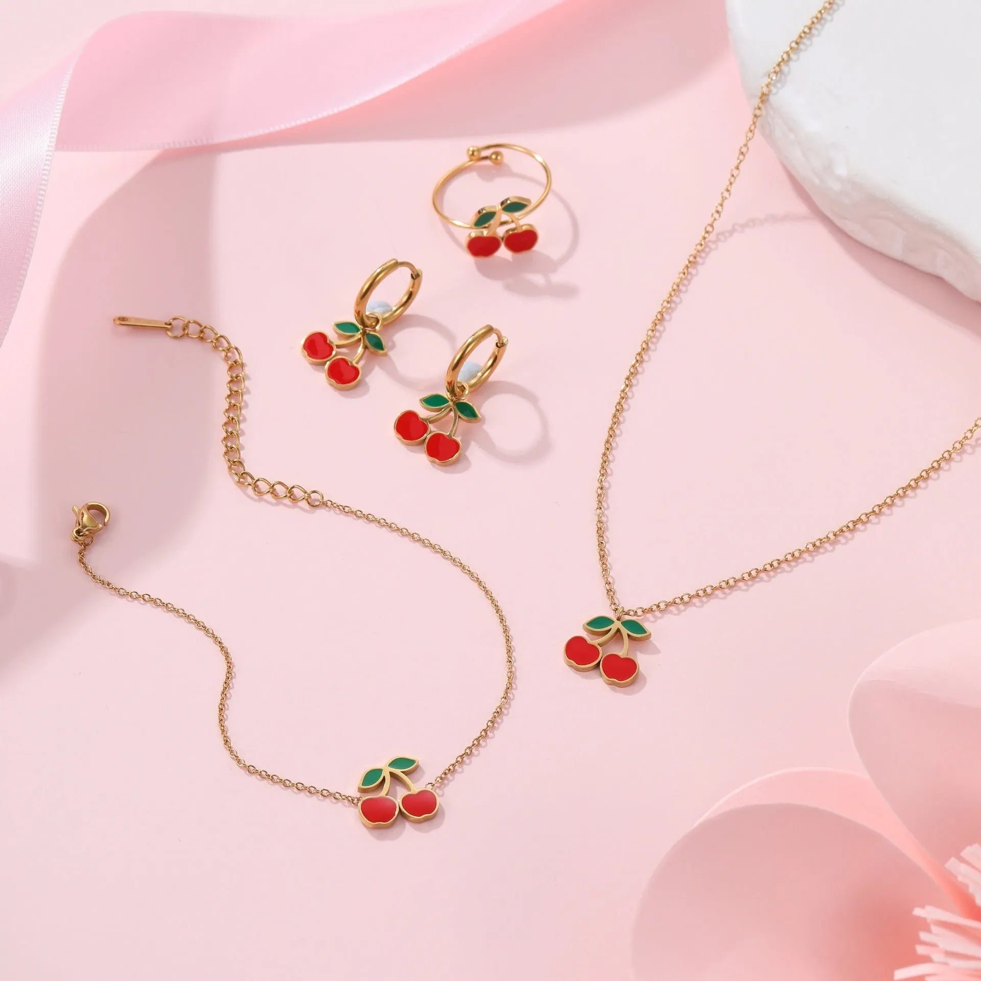 Cherry-themed jewellery set with gold-plated necklace, bracelet, earrings, and ring on stainless steel chains.