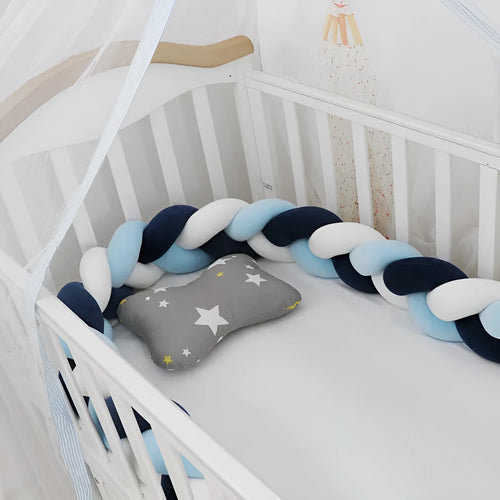 Braided knot style baby crib bumper in a light grey colour, shown lined inside a white wooden cot.