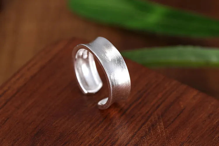Geometric open ring with adjustable size in frosted sterling silver on a grey background.