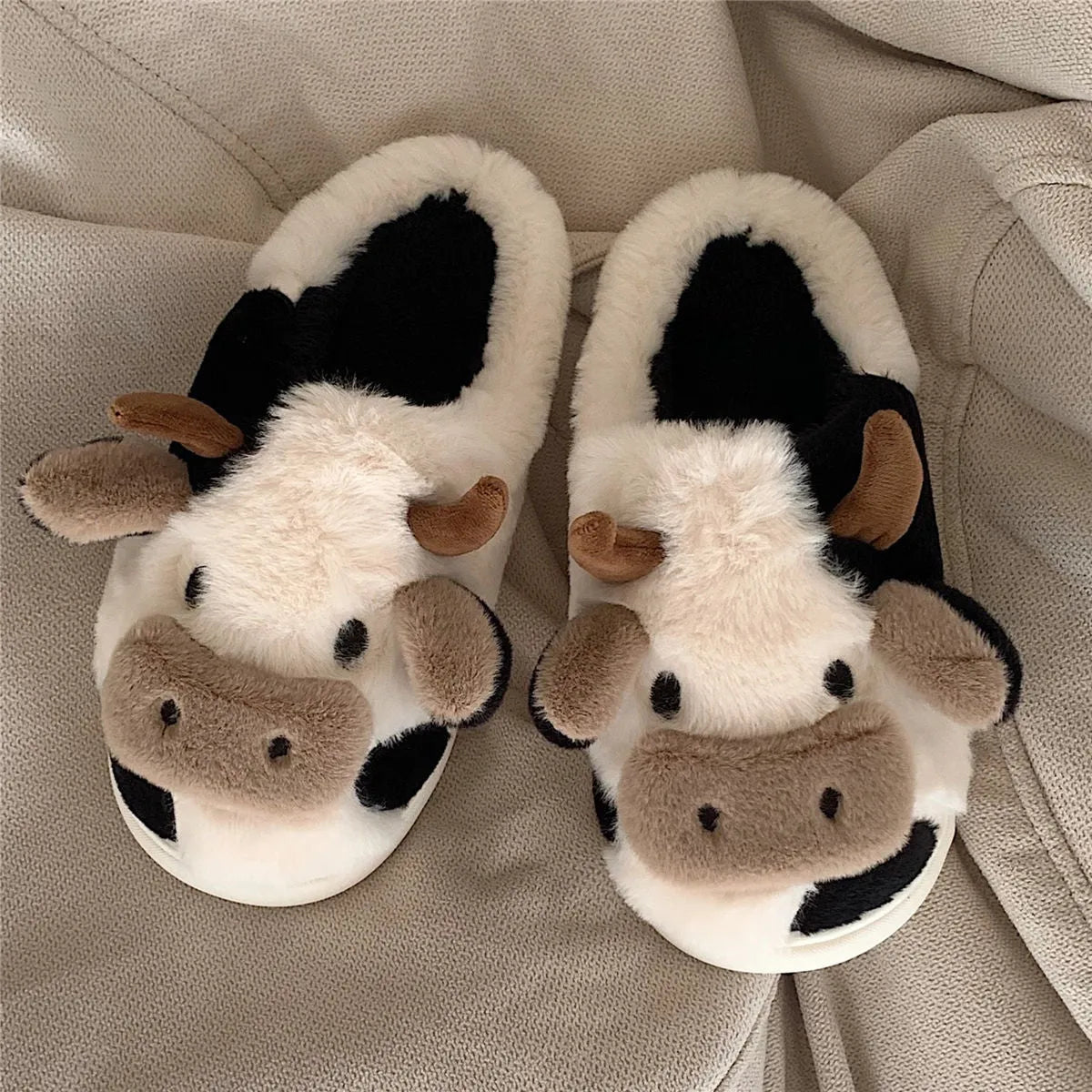 White cow-themed faux fur slippers with plush lining and textured non-slip soles.