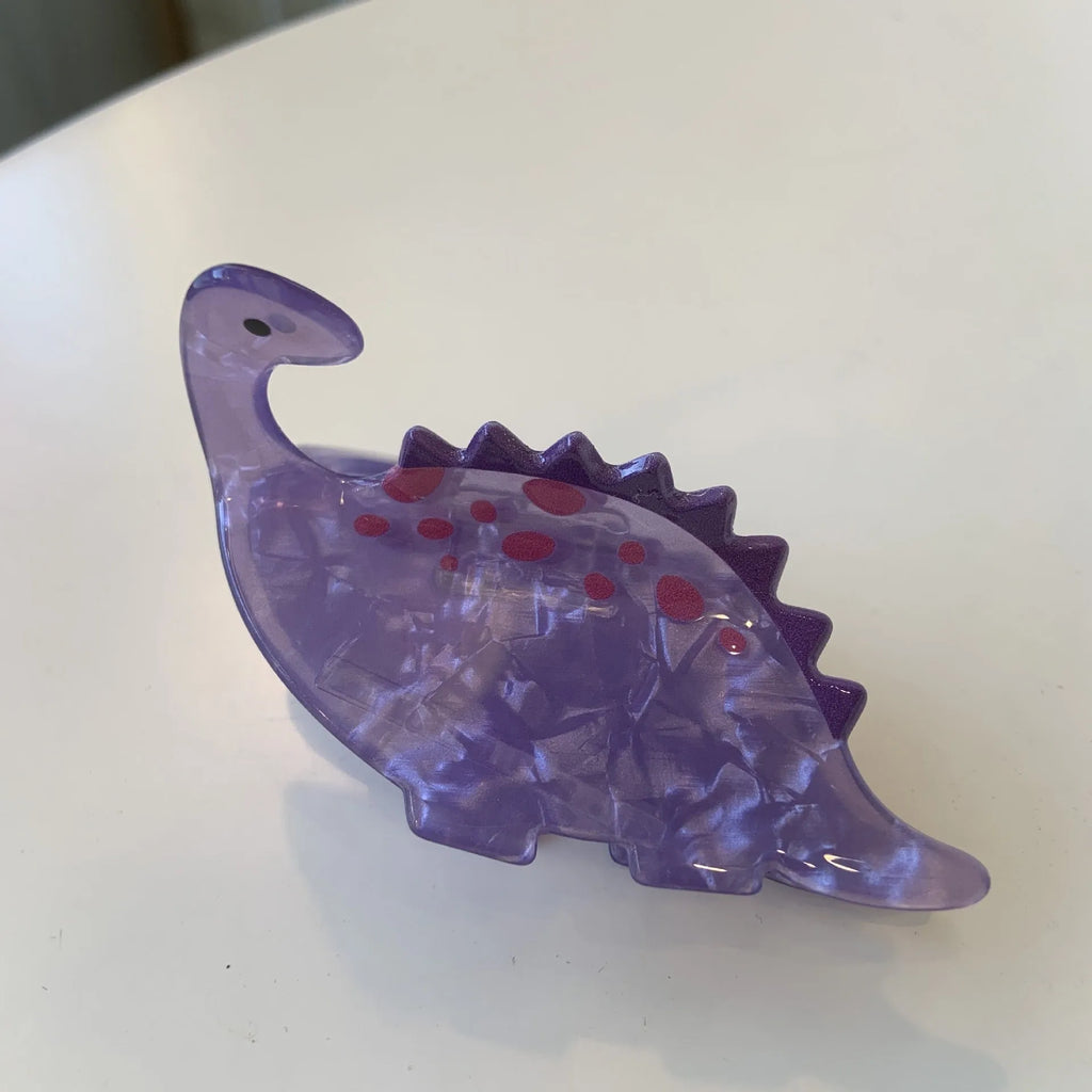 Acrylic dinosaur jaw clip hairpin showing one of six colour designs: Pink Pterosaur, Green Stegosaurus, Purple Dragon, Blue Dinosaur, Brown Tyrannosaurus, or Green Chameleon.