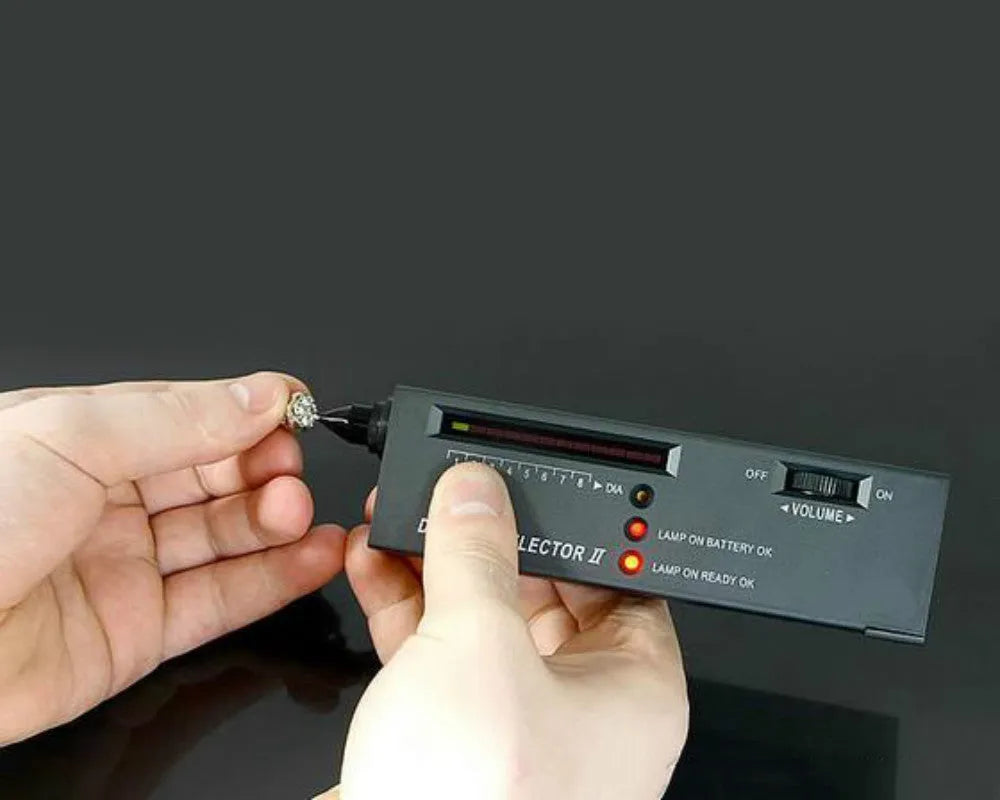 Handheld black diamond thermal conductivity tester with metal probe on a gemstone.