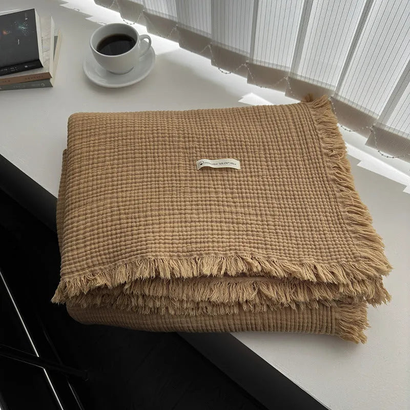 Four-layer gauze cotton blanket with tassel trim in avocado green colour draped over a sofa