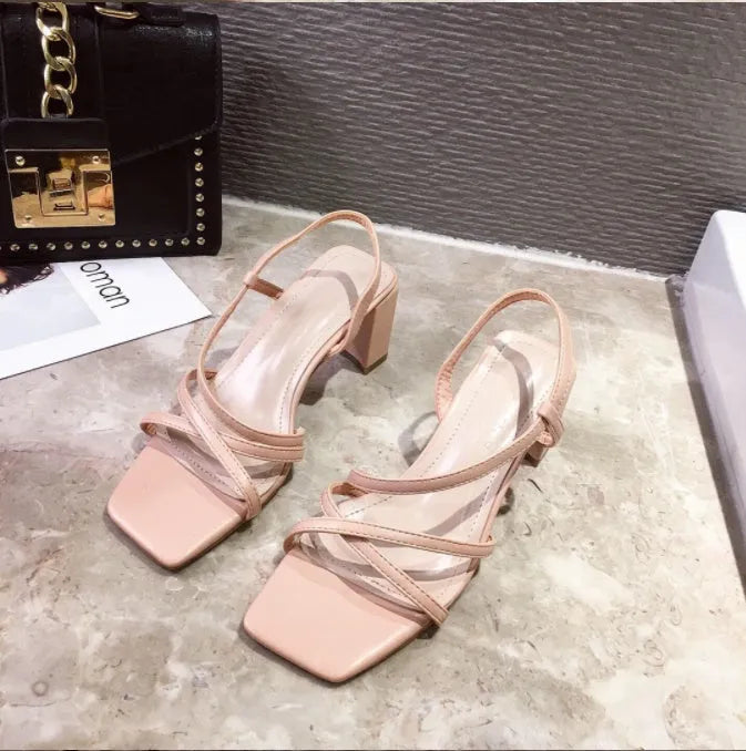 Women's white thick heel sandals with a backless design and side cut-outs on a wooden floor.