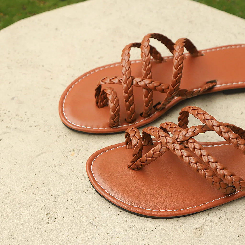 White women's clip-toe woven flat sandals with a rubber sole on a wooden floor.