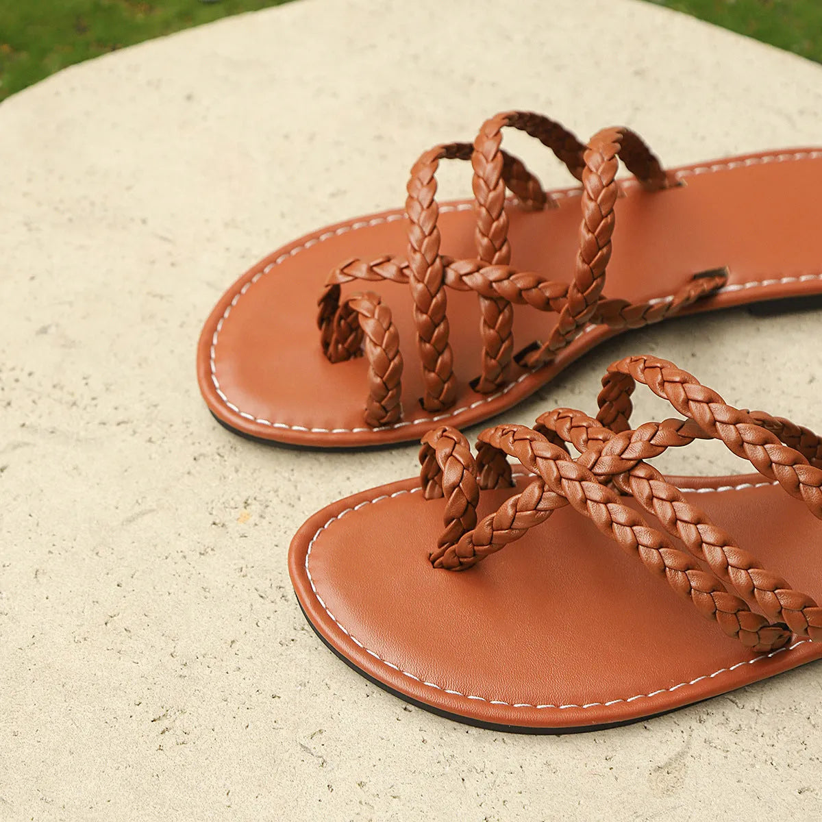 White women's clip-toe woven flat sandals with a rubber sole on a wooden floor.