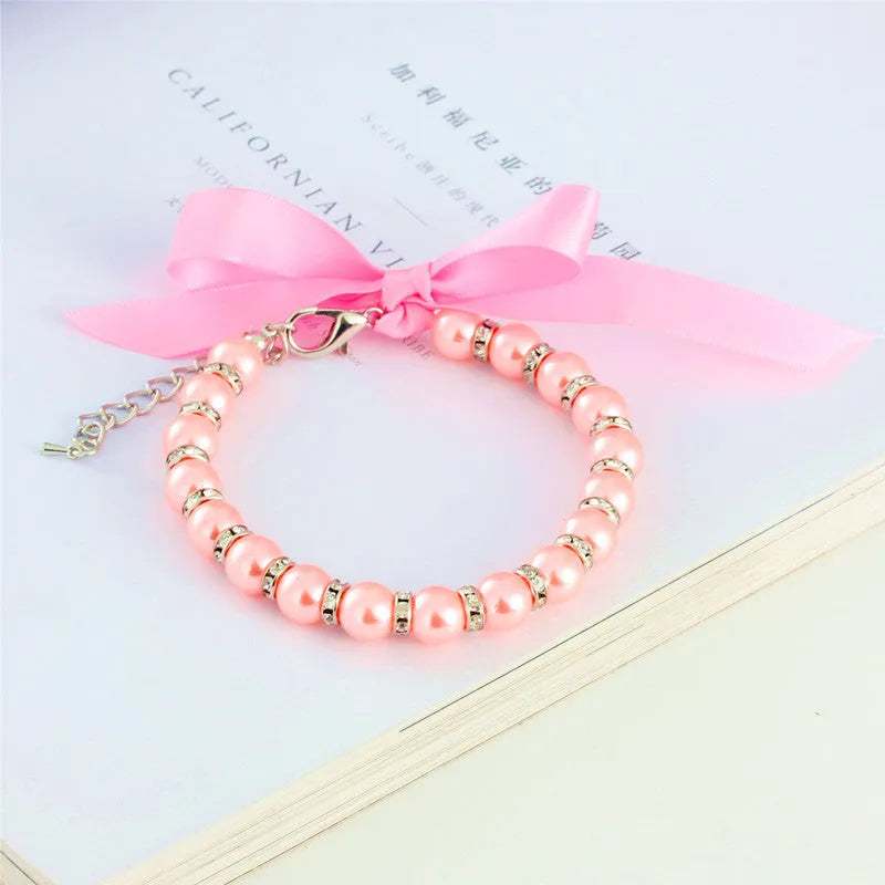 Small dog wearing blue imitation pearl and rhinestone necklace with adjustable clasp and ribbon bow