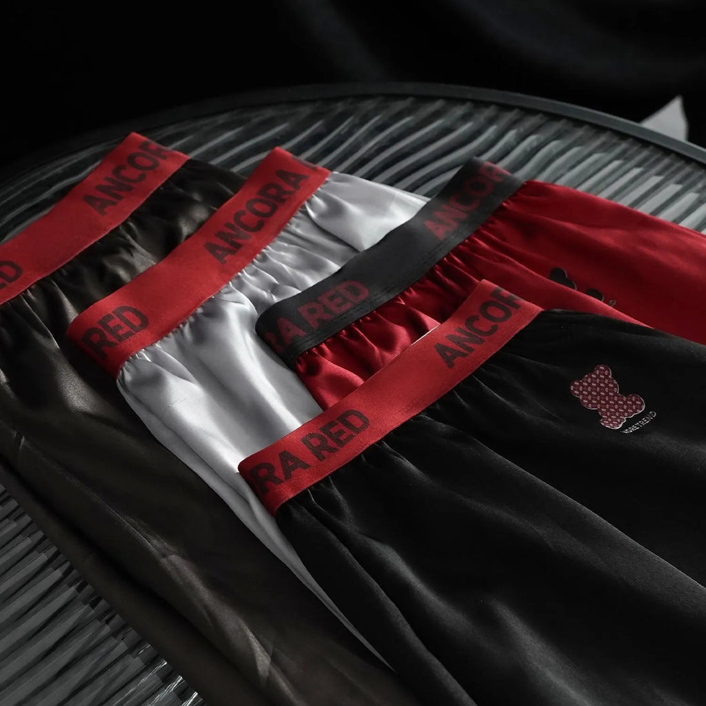 Solid colour men's boxer briefs on a mid-waist model, showing polyester knit fabric in black, blue, red, silver, purple and brown.