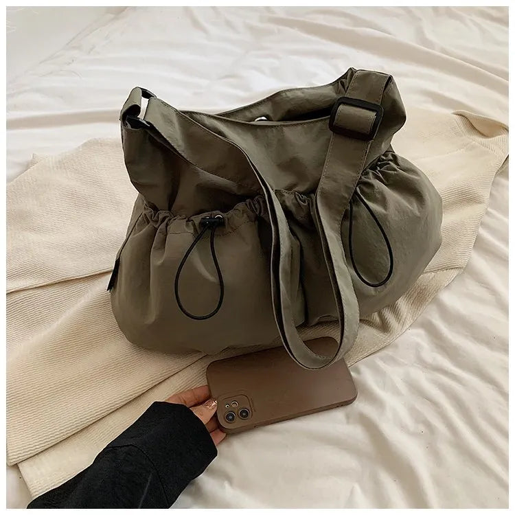 Ultra-light pleated green crossbody cloth bag lying flat, showing its split pocket and foldable design.