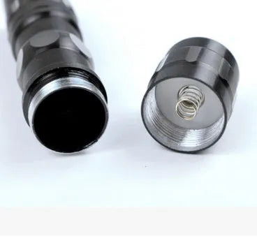 Black aluminium alloy mini LED handheld flashlight next to a AA battery